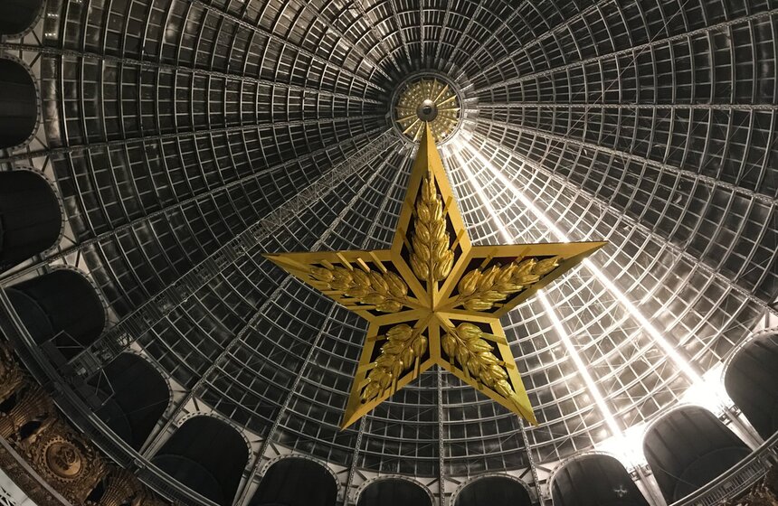 Фото: АГН Москва. Монтаж люстры-звезды в павильоне "Космос" на территории ВДНХ. 17 ноября люстру-звезду из рубинового стекла − точную копию той, которая в середине 30-х годов прошлого века украшала Троицкую башню Кремля, – установили под куполом павильона "Космос" на ВДНХ. Ее укрепили на высоте 36 метров. Каркас новой люстры выполнен из черного металла, а металлические лучи светильника снабжены вставками из стекла рубинового оттенка. К ним крепятся декоративные колосья пшеницы из латуни. Кроме стеклянных вставок, вся остальная поверхность осветительного прибора покрыта сусальным золотом. В люстру встроено 60 энергоэффективных светодиодных ламп теплого белого света, мощность которых составляет 100 ватт.<br /><br />АГН Москва