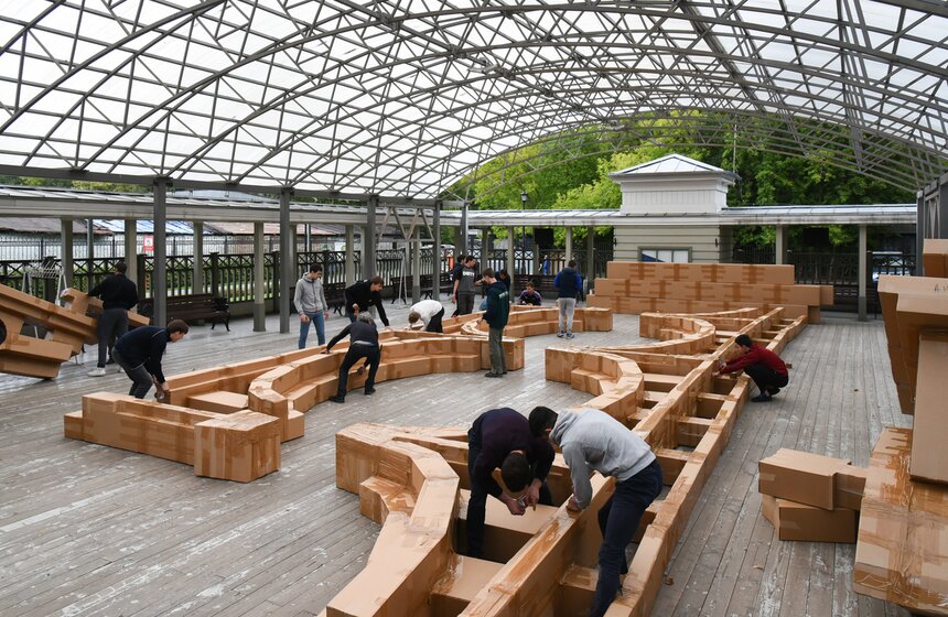 В это время под навесом десяток человек вместе с Гросстетом и несколькими его помощниками скрепляли составные части моста. Основа конструкции – картонные коробки, приклеенные друг к другу скотчем по определенной технологии. Они должны быть определенного веса и формы – поэтому для работы их доставляли на заказ. Всего, по словам организаторов, потребовалось более трехсот коробок. Количество скотча никто даже не пытался подсчитать.