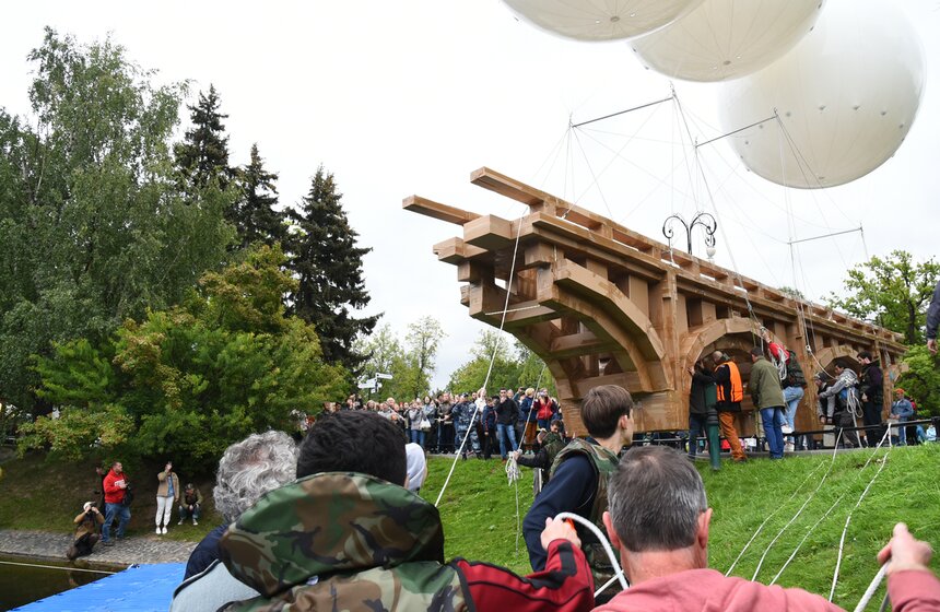 Сначала мост с шарами опустили на поддон, а затем отправили в центр пруда. Направляли процесс и с берега, с помощью канатов, и на воде: несколько волонтеров сопровождали мост на лодках.