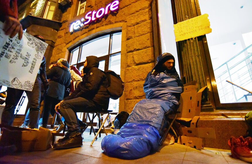 Вдоль витрины магазина расставлены раскладные походные стулья, некоторые спят сидя. Кто-то постелил себе несколько пледов и лежит на земле, несмотря на холодную погоду.
